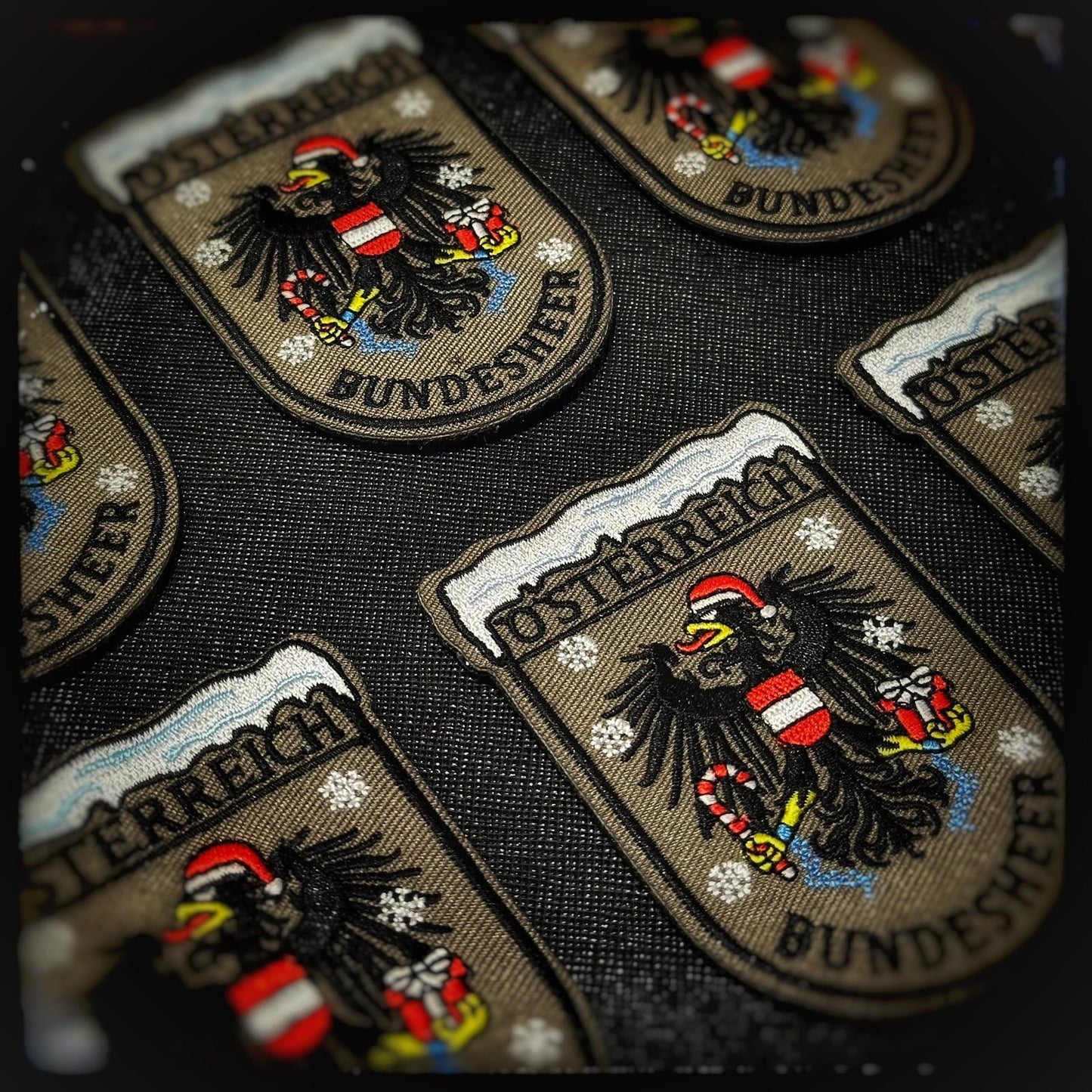 Gewebter Patch mit Klett: Bundesheer Weihnachtsadler. Österreichs stolzestes Wappentier zeigt sich weihnachtlich: der Bundesheer-Adler mit Nikolausmütze, Geschenk in der einen Kralle und Zuckerstange wie eine festliche Seitenwaffe in der anderen. Wachsam wie immer – nur kurz im Einsatz zum Schutz von Weihnachten. Hochwertige und langlebige 3D PVC, gewebte und gestickte Patches für Sammler, Airsofter und Militärangehörige. Dient auch als Moral-Patch. Patchworld.net. patchworld