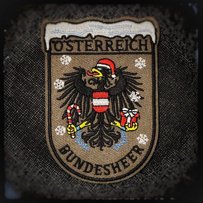 Gewebter Patch mit Klett: Bundesheer Weihnachtsadler. Österreichs stolzestes Wappentier zeigt sich weihnachtlich: der Bundesheer-Adler mit Nikolausmütze, Geschenk in der einen Kralle und Zuckerstange wie eine festliche Seitenwaffe in der anderen. Wachsam wie immer – nur kurz im Einsatz zum Schutz von Weihnachten. Hochwertige und langlebige 3D PVC, gewebte und gestickte Patches für Sammler, Airsofter und Militärangehörige. Dient auch als Moral-Patch. Patchworld.net. patchworld