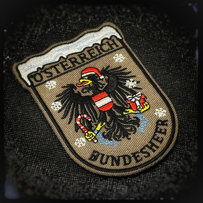 Embroidered Patch with velcro: Bundesheer Christmas eagle. Austria’s fiercest symbol has gone festive: the Bundesheer eagle in a Santa hat, holding a present and a sugar cane like a seasonal sidearm. Still proud, still vigilant—just temporarily reassigned to defend Christmas with maximum discipline and holiday cheer. High quality and durable PVC, woven and embroidered patches for collectors, airsofters and military enthusiasts. Also serves as a morale patch. Patchworld.net. patchworld